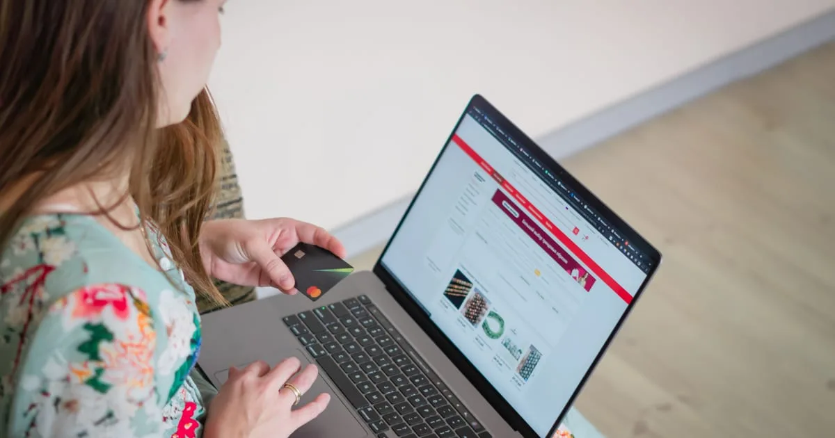 Shopper holding a credit card while paying for an online order on a laptop at home