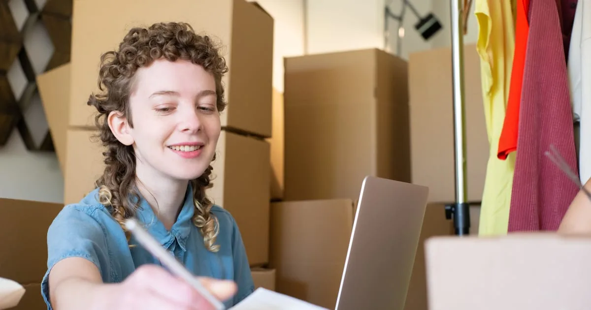 Small online store owner checking orders and website settings on a laptop beside packed parcels