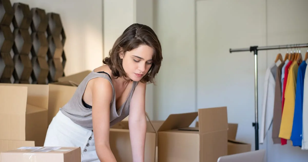Small business owner packing a customer order beside a laptop at a home workspace