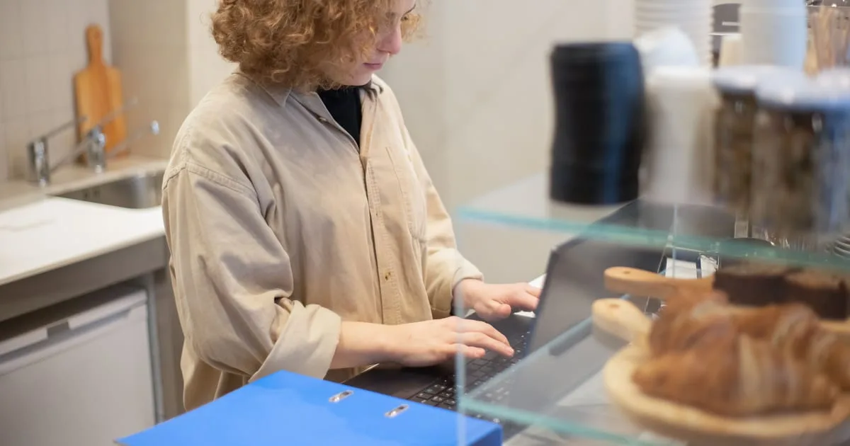 Small business owner reviewing customer follow-ups on a laptop at a shop counter