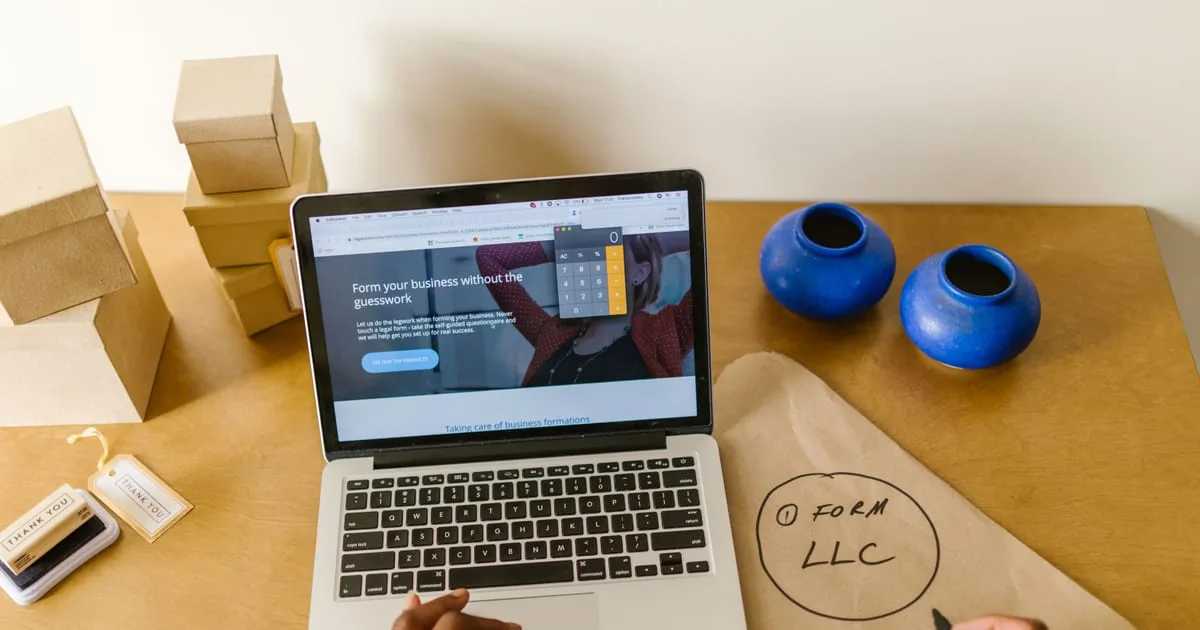 Small business owner working on a laptop at a studio desk with product stock on shelves behind